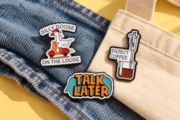 Silly Goose, Inject Coffee and Talk Later enamel pin designs styled on blue denim and cream canvas