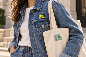 BELIEVE pin on a denim jacket and Spreadsheet pin on a cream canvas tote