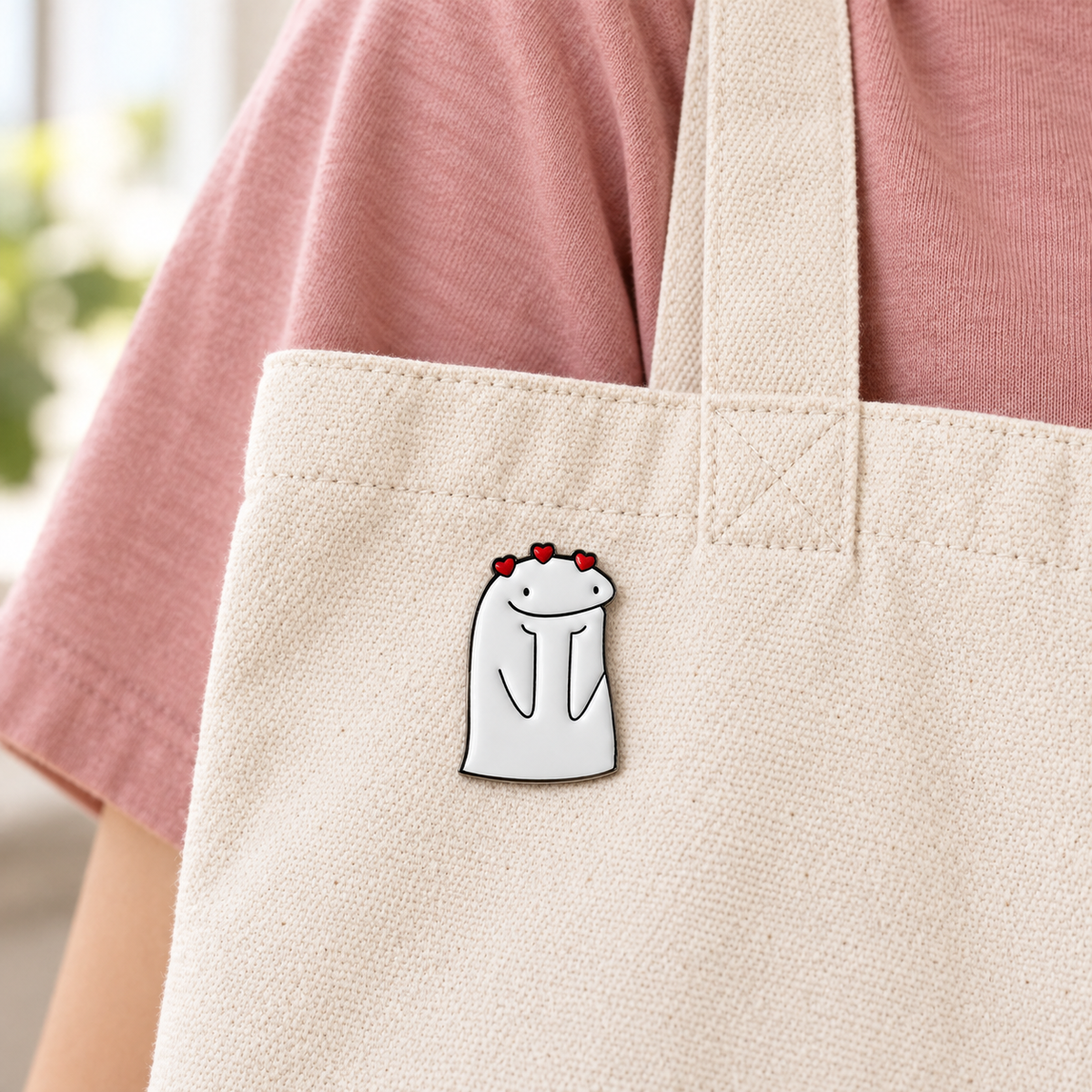 AI-styled wearing view of Three Hearts Smiling Character Pin on cream cotton canvas tote being carried on an adult's shoulder over a dusty-rose shirt