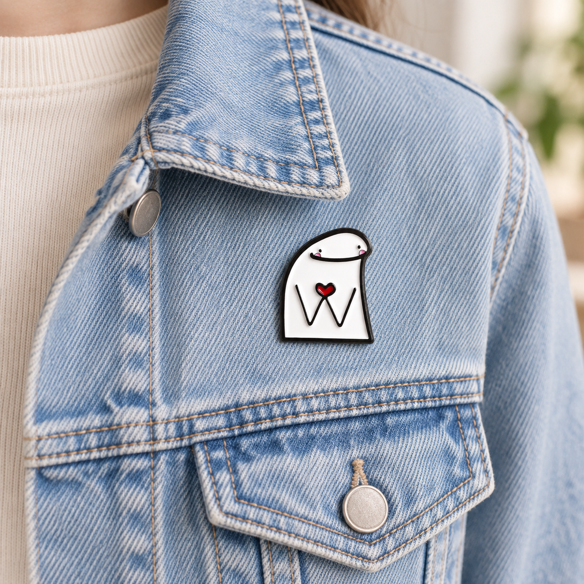 AI-styled wearing view of Smiling Character Holding Red Heart Pin on light blue denim jacket being worn by an adult over ivory cotton. Pin near upper chest beside a full normal 13cm-wide chest pocket