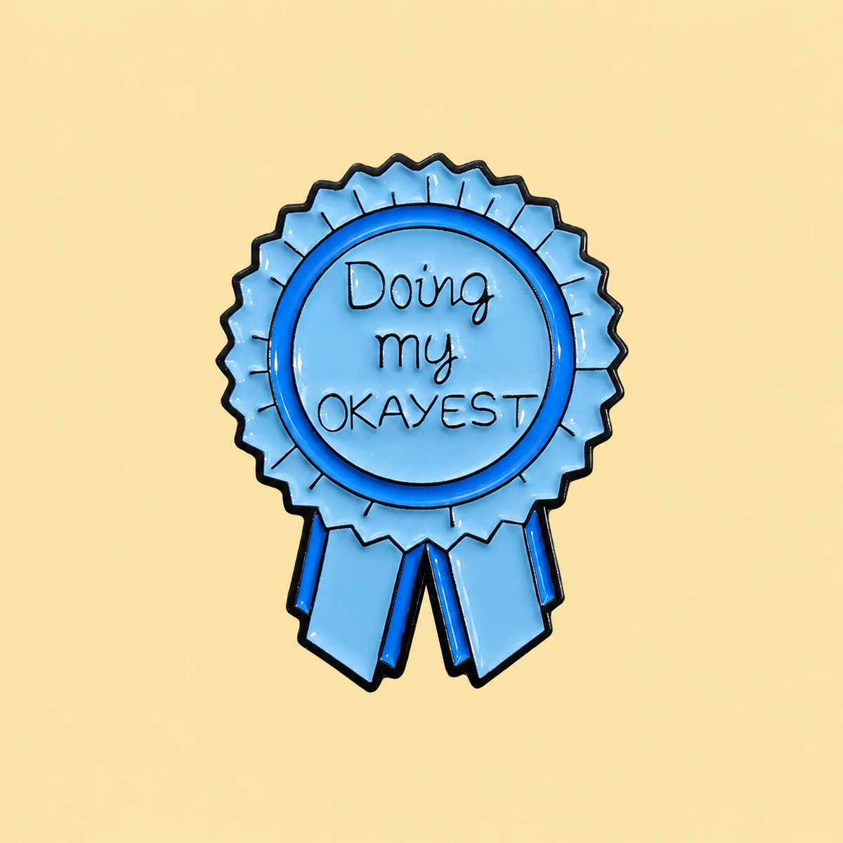 Blue Doing My Okayest award ribbon enamel pin on a pale butter yellow background