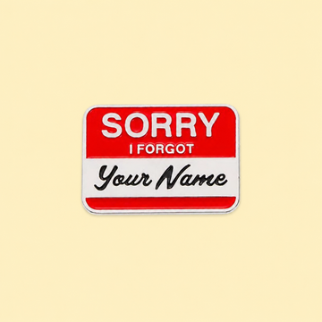 Red-and-white Sorry I Forgot Your Name enamel pin on a soft pale yellow background