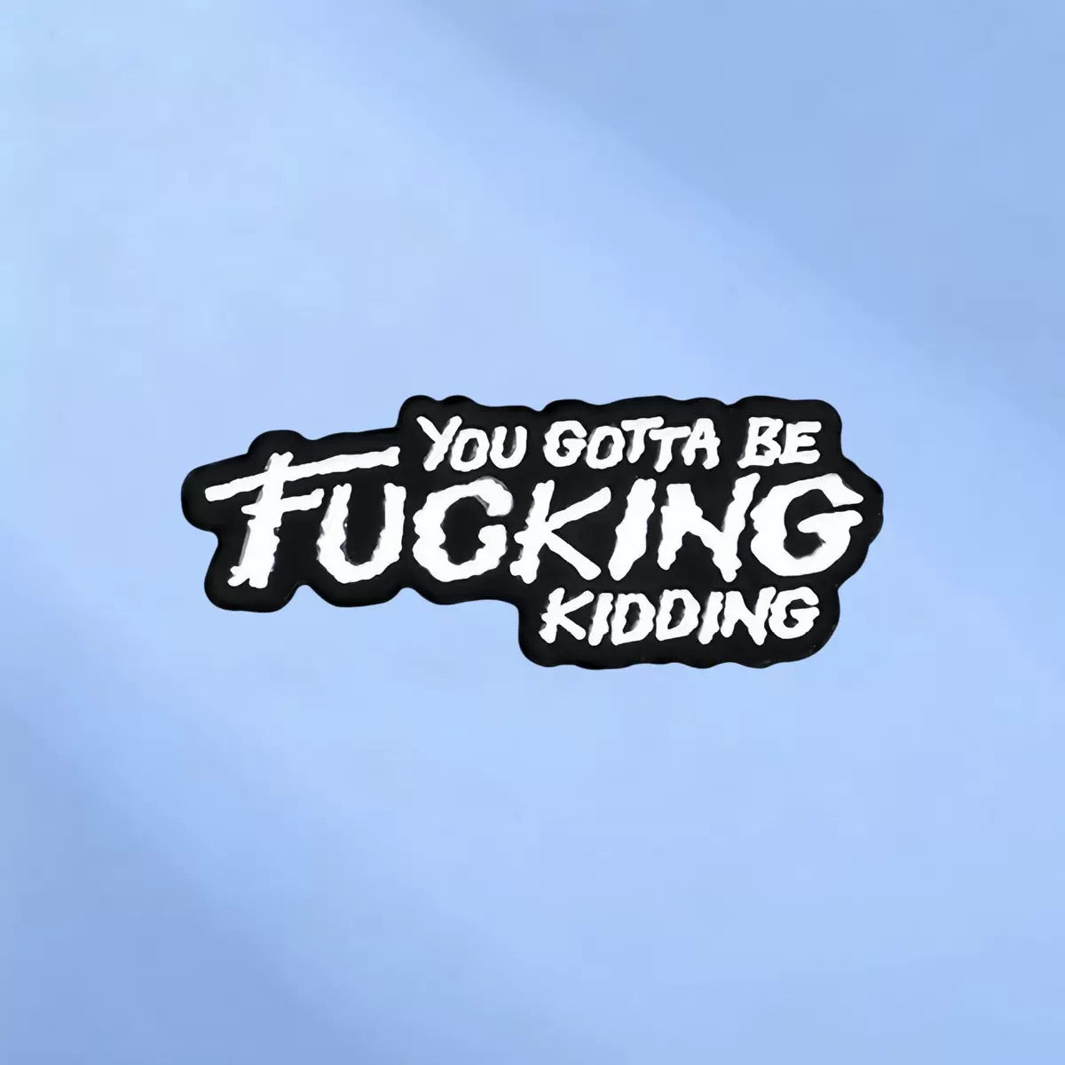 Black enamel statement pin with white You Gotta Be Fucking Kidding lettering on a blue background