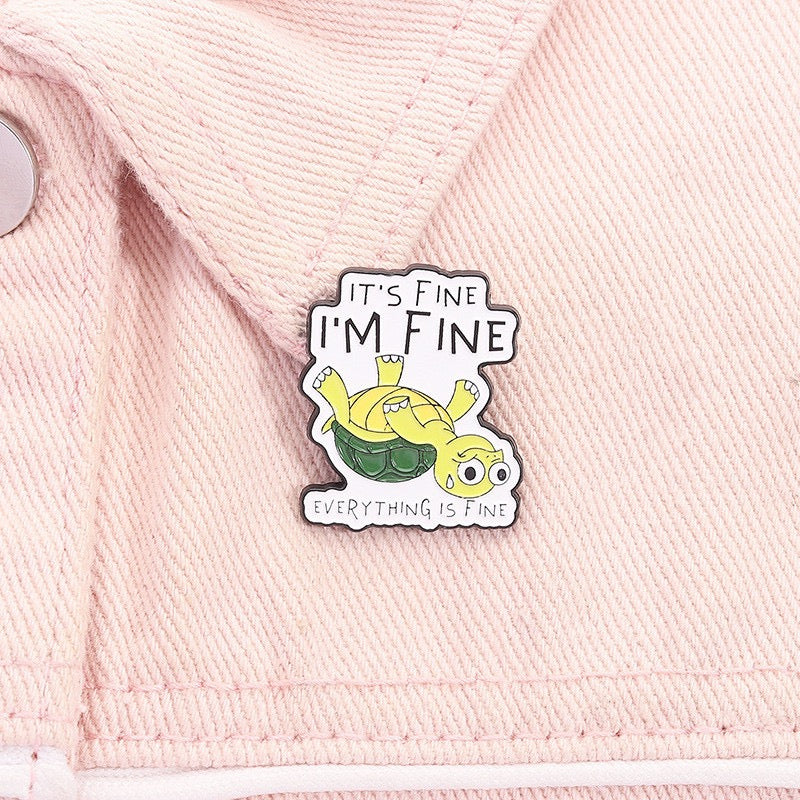 It's Fine, I'm Fine Upside-Down Turtle Enamel Pin worn on a pink shirt