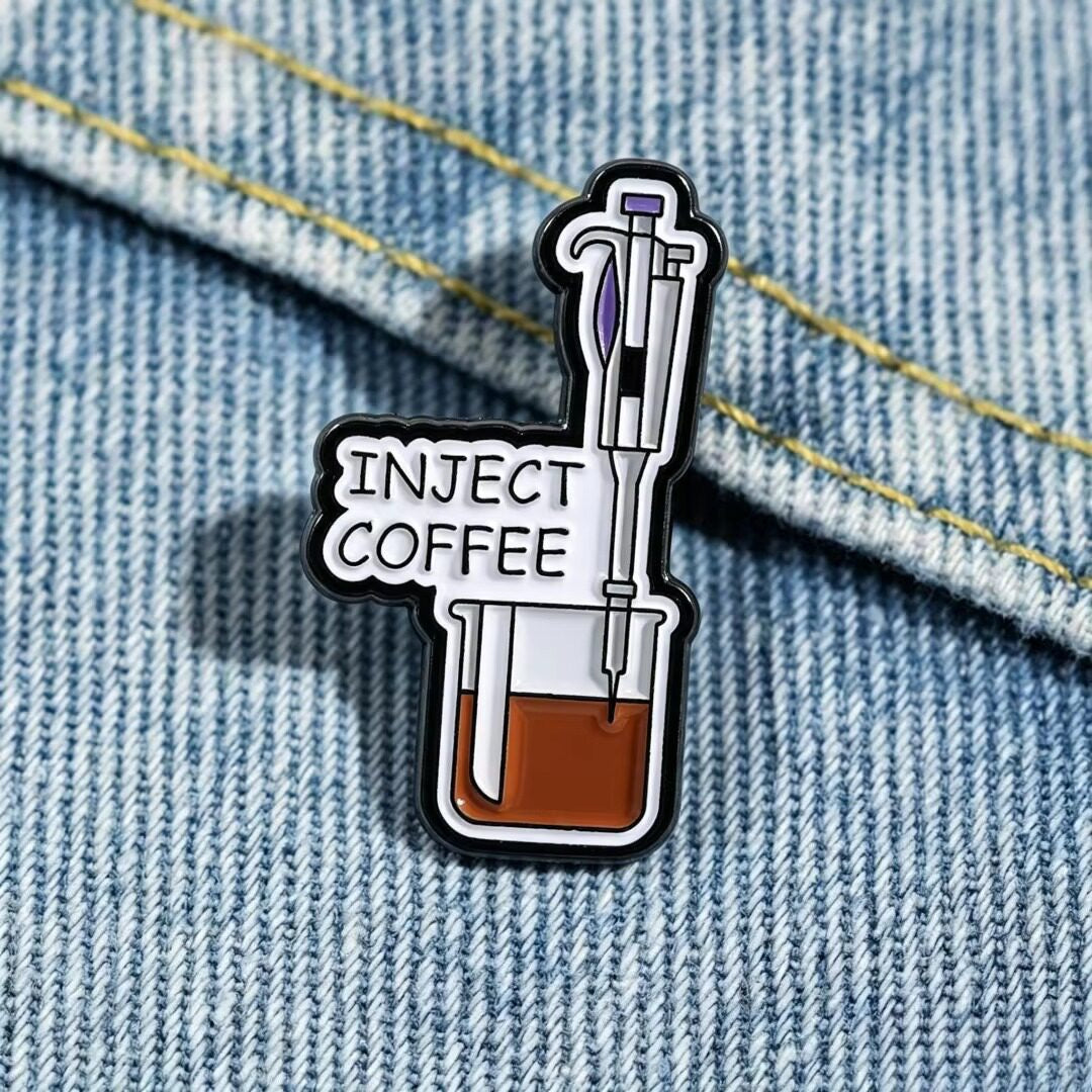 Inject Coffee enamel pin showing a purple-accented syringe above a coffee-filled beaker on blue