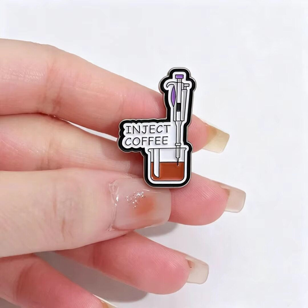 Inject Coffee Syringe Enamel Pin held between fingers for scale