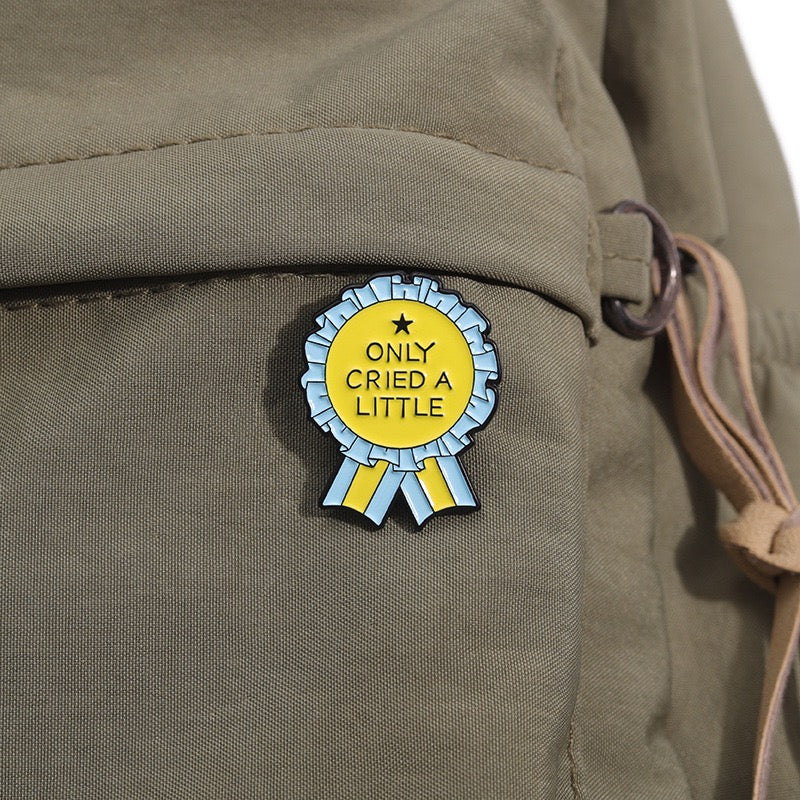 Yellow and light blue Only Cried a Little enamel pin on an olive backpack
