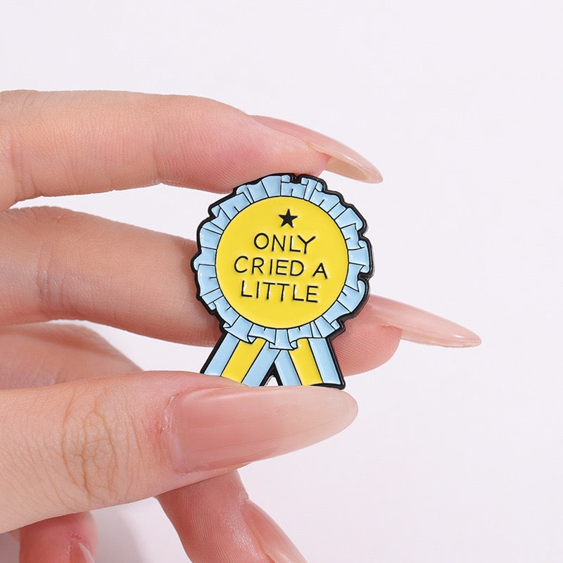 Only Cried a Little rosette enamel pin held between fingers for scale