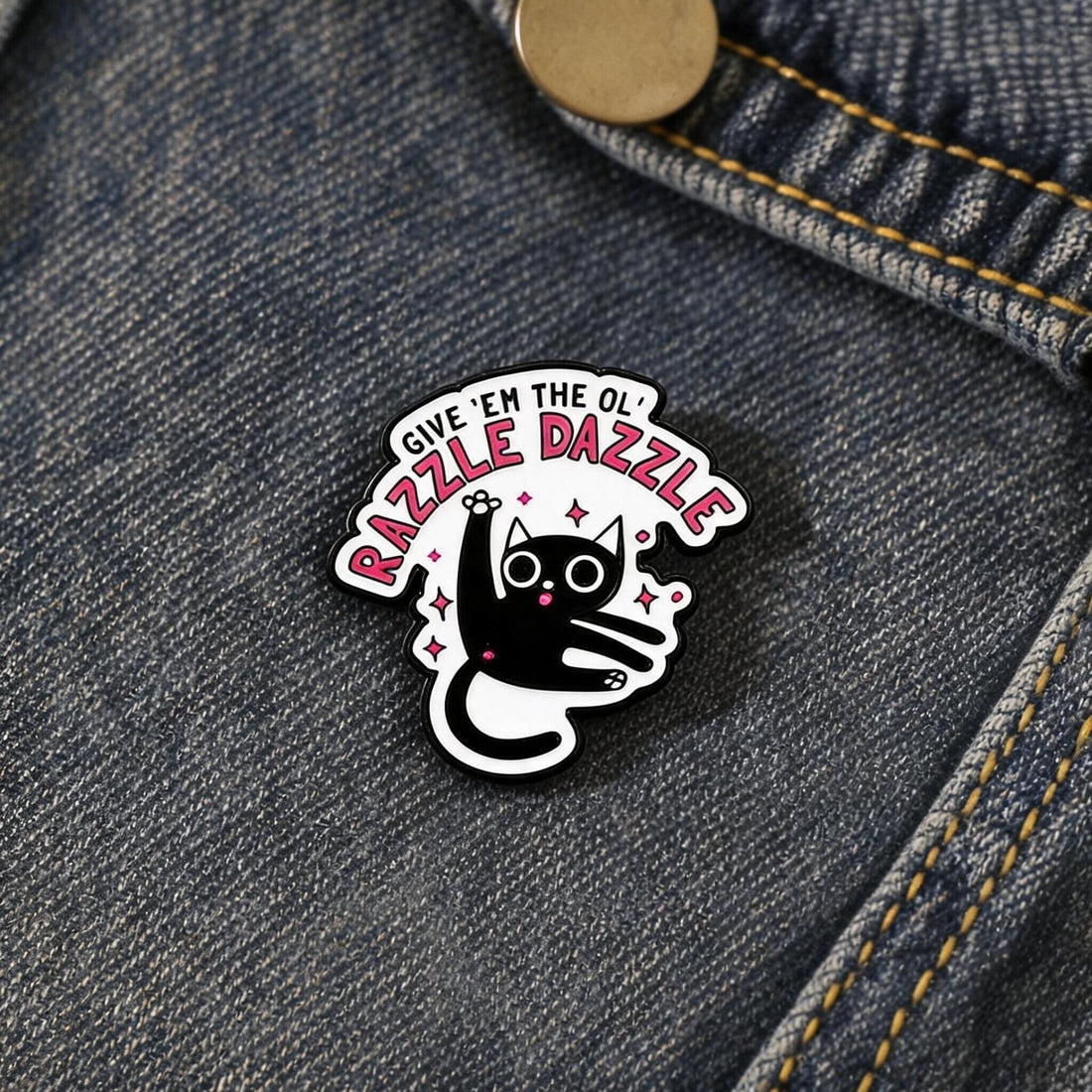 Black-and-white cat enamel pin with Give 'Em the Ol' Razzle Dazzle lettering and pink sparkles on yellow