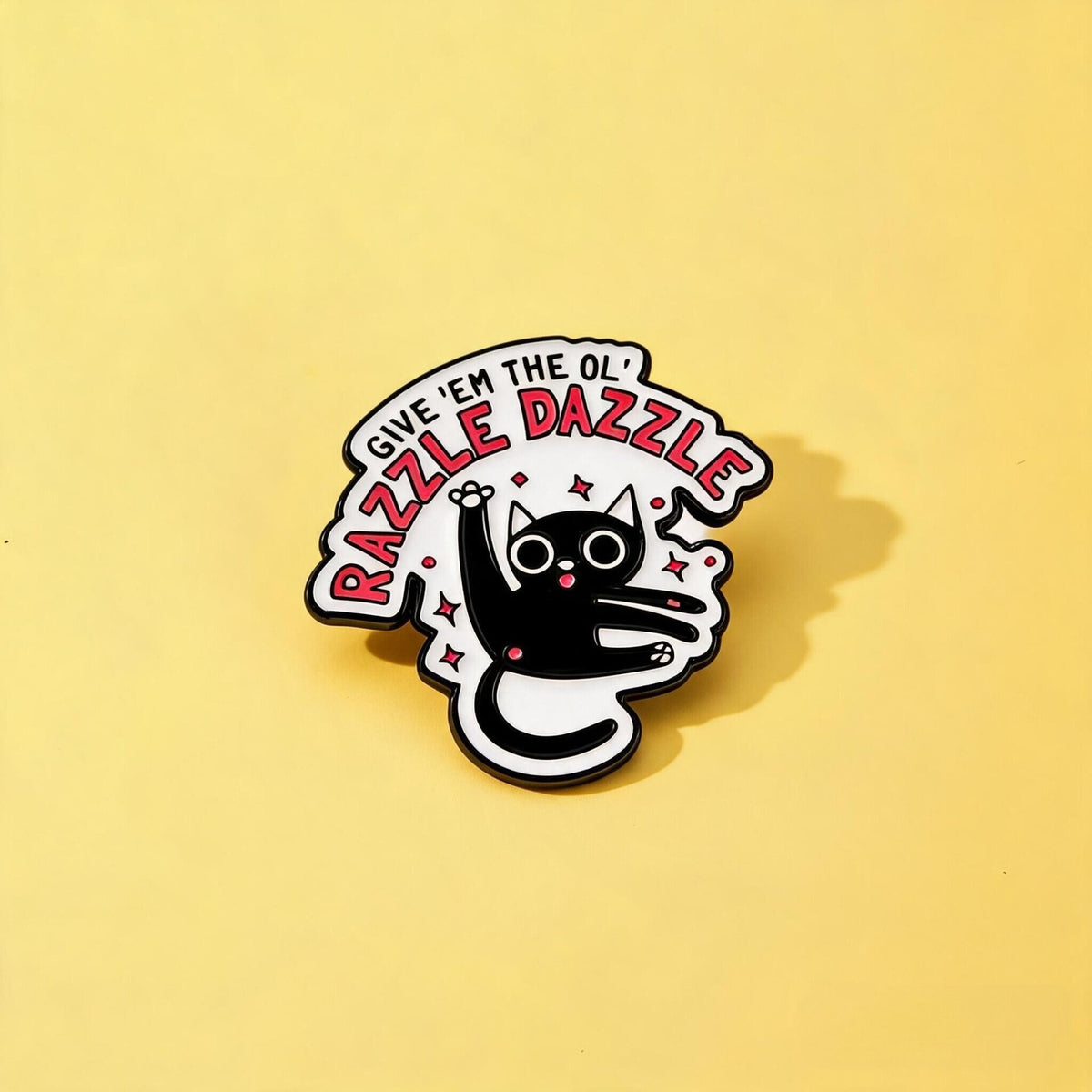 Black-and-white cat enamel pin with Give 'Em the Ol' Razzle Dazzle lettering and pink sparkles on yellow