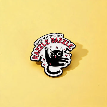 Black-and-white cat enamel pin with Give 'Em the Ol' Razzle Dazzle lettering and pink sparkles on yellow