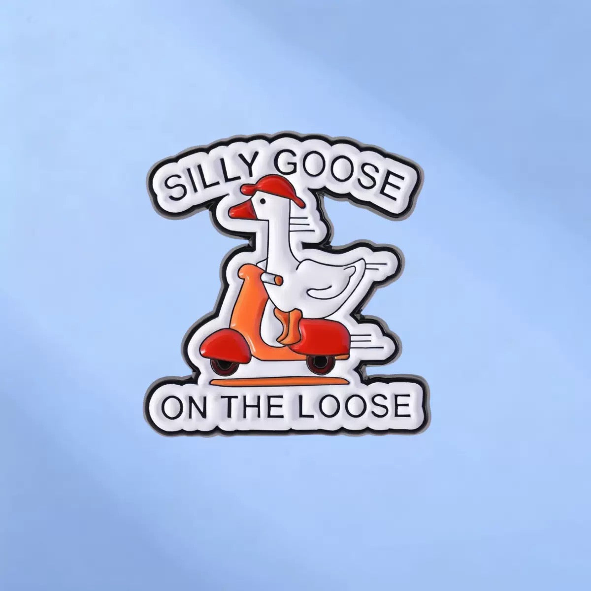 White goose riding a red scooter enamel pin reading Silly Goose on the Loose on a blue background