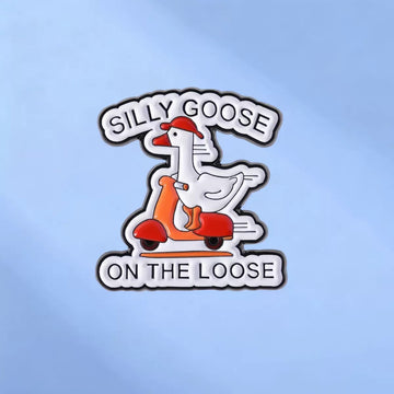 White goose riding a red scooter enamel pin reading Silly Goose on the Loose on a blue background