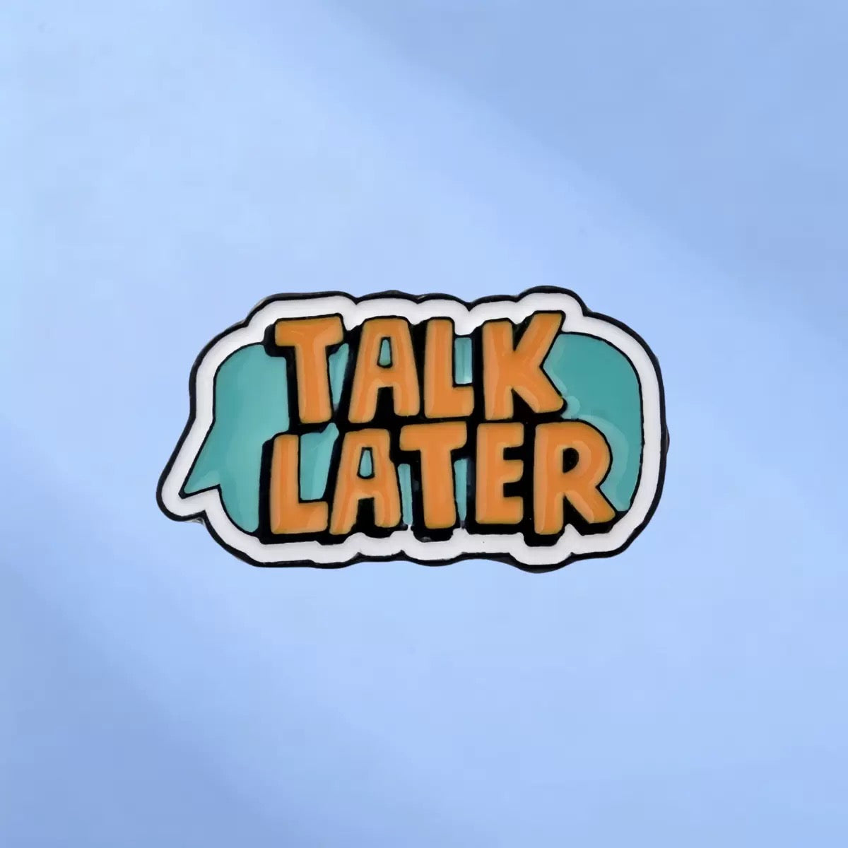 Turquoise speech bubble enamel pin with orange Talk Later lettering on a blue background