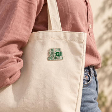 Green Spreadsheet enamel pin on a cream canvas tote with a rose cotton shirt